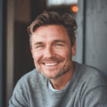 Homme souriant avec pull gris, intérieur moderne.